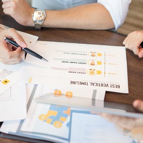 Close-up of businessman reading reports and discussing them with female colleague. Hands of male and female colleagues sitting at table and working together. Cooperation and teamwork concept